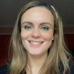 Professora Doutora Karen Ambra Imagem de uma mulher branca, loira de cabelos lisos, sorrindo com um fundo escuro.